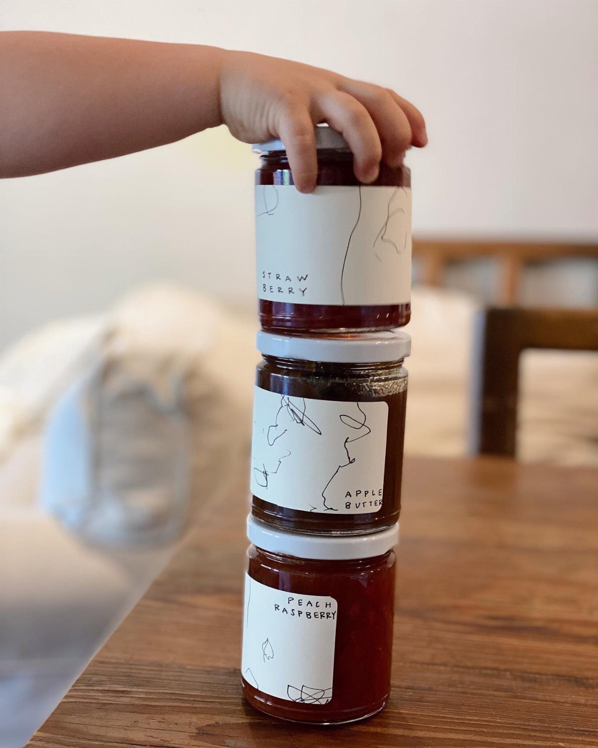 Three stacked glass jars of homemade jam with minimalist labels on a wooden table.
