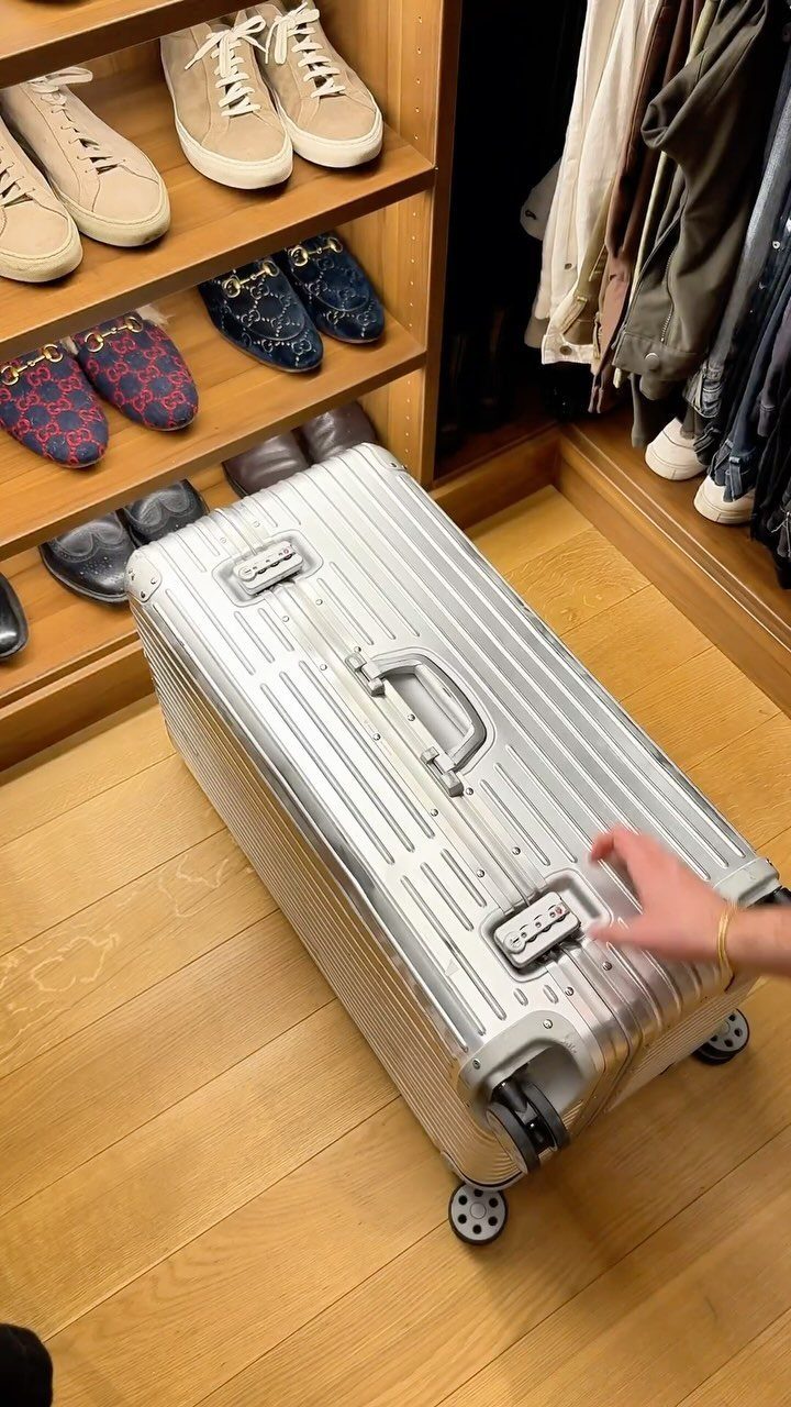 Silver aluminum suitcase on a wooden floor in a luxury men's walk-in closet