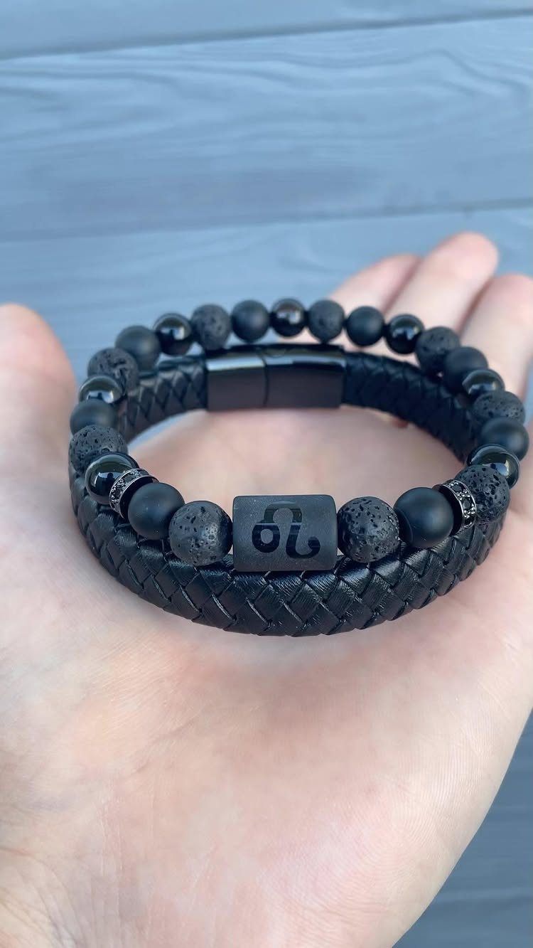 Black braided leather and bead bracelet held in a person's open palm.