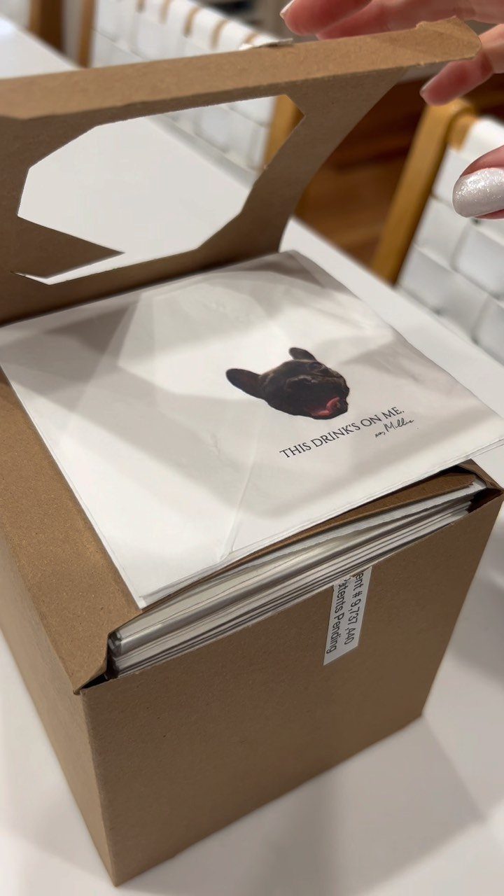 Custom white cocktail napkins with a black dog photo inside a cardboard box.