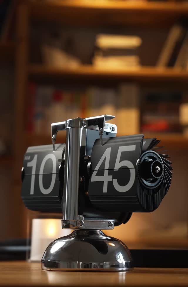 Mechanical desk clock with rotating black drums and polished chrome frame on wood.