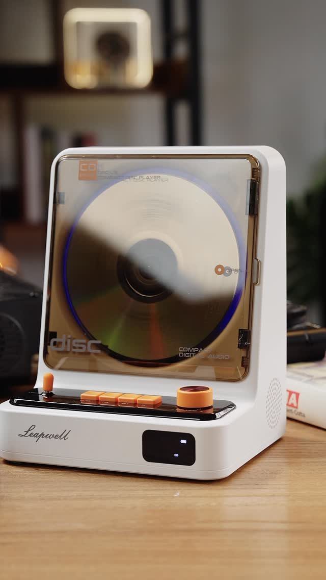White modern CD player with transparent cover and orange buttons on wooden table