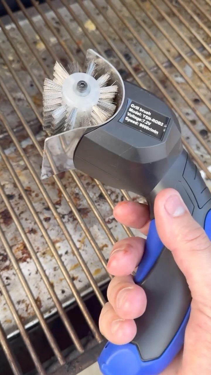 Motorized grill brush with blue handle cleaning a metal grill grate