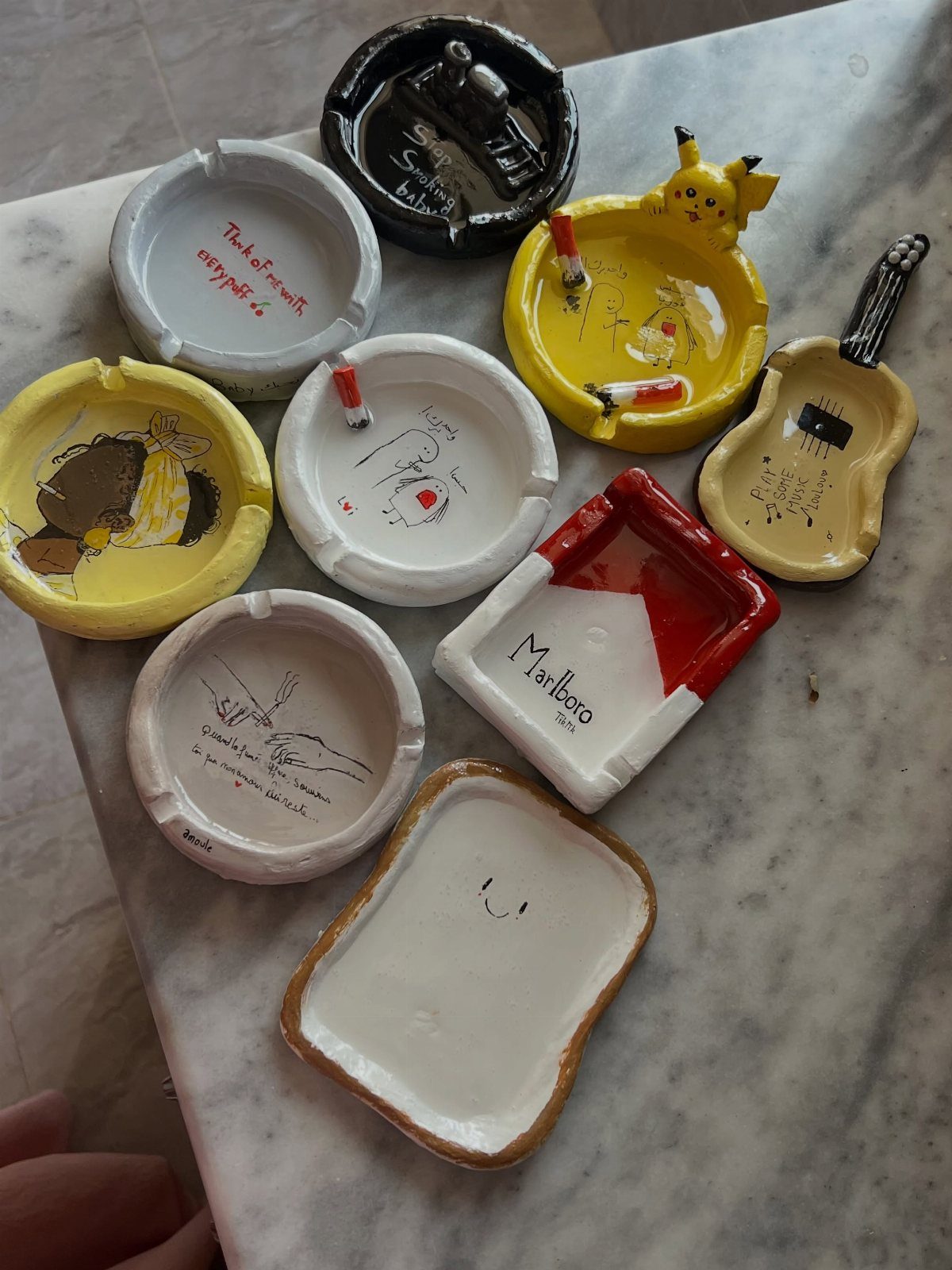 Handmade ceramic ashtrays in various shapes and colors on a white marble surface.