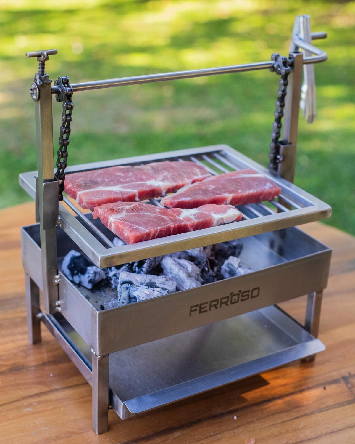 Stainless steel portable grill with raw steaks over hot charcoal on wooden table