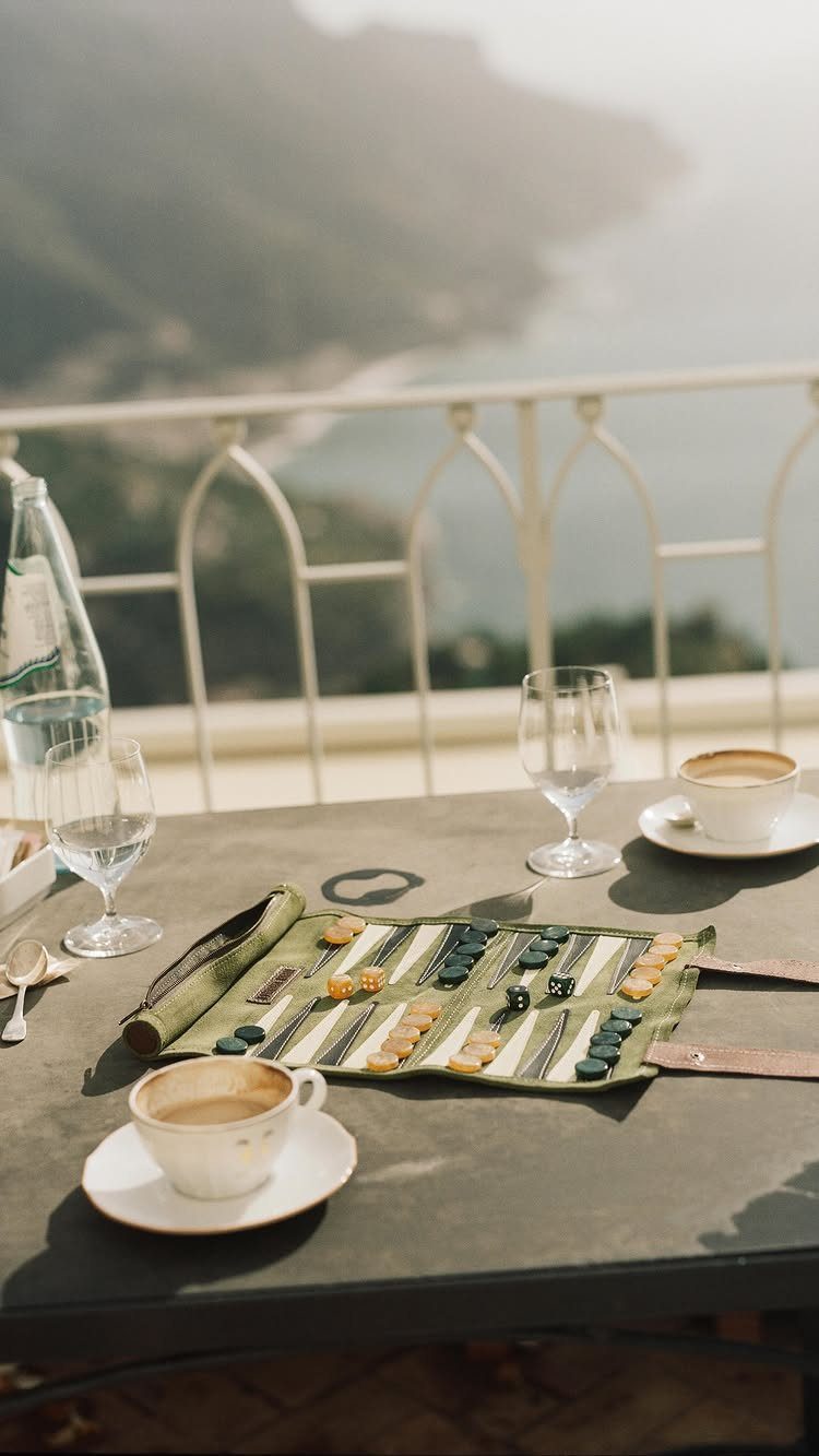 Travel backgammon set on a cafe table overlooking a coastal mountain landscape