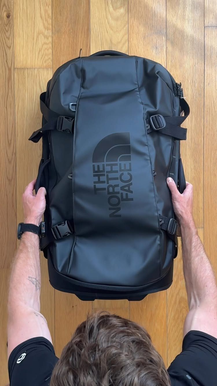 Black The North Face duffel bag held by a person on wooden flooring