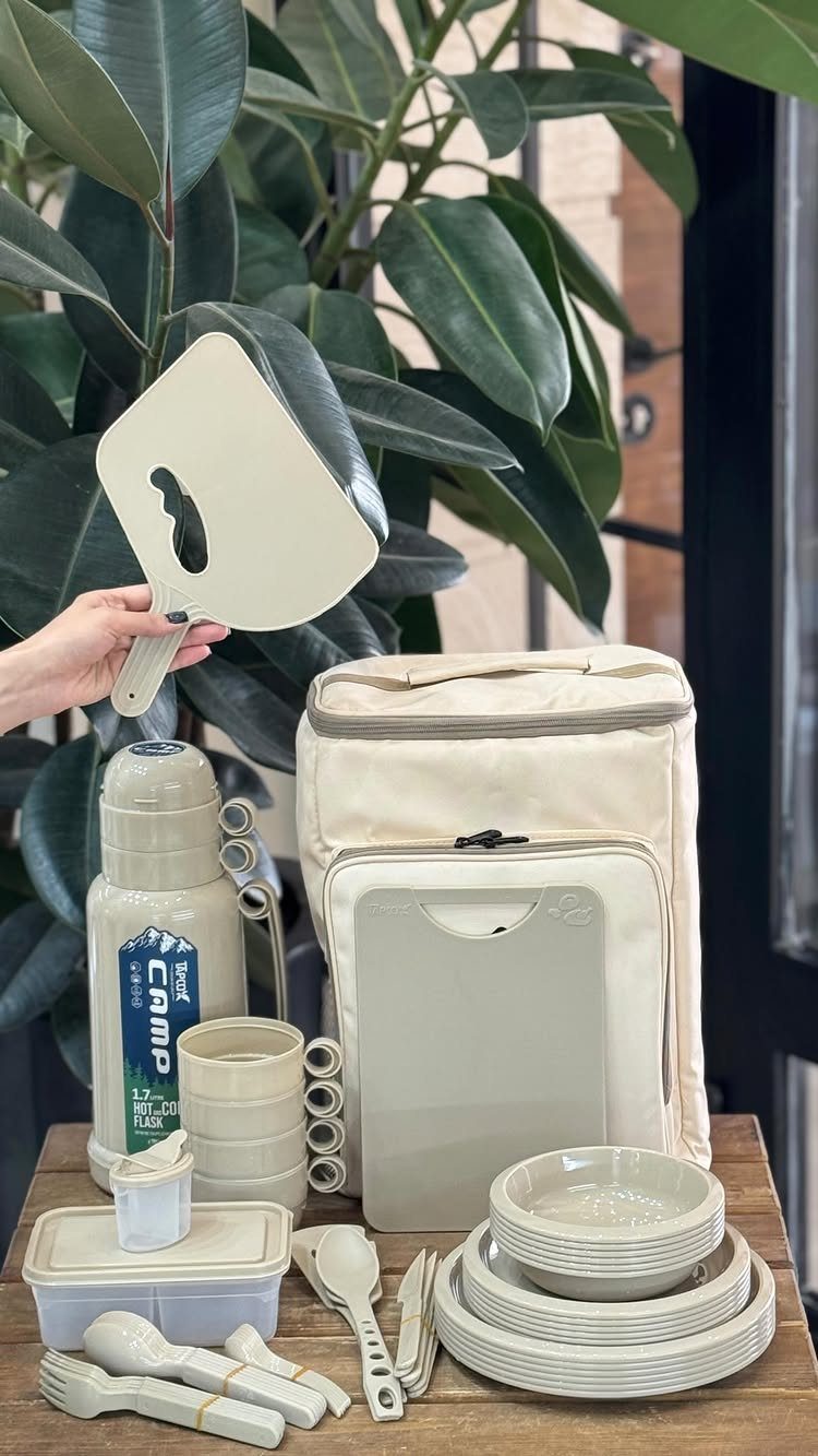 Beige camping cookware set with thermal flask and plates on a wooden table