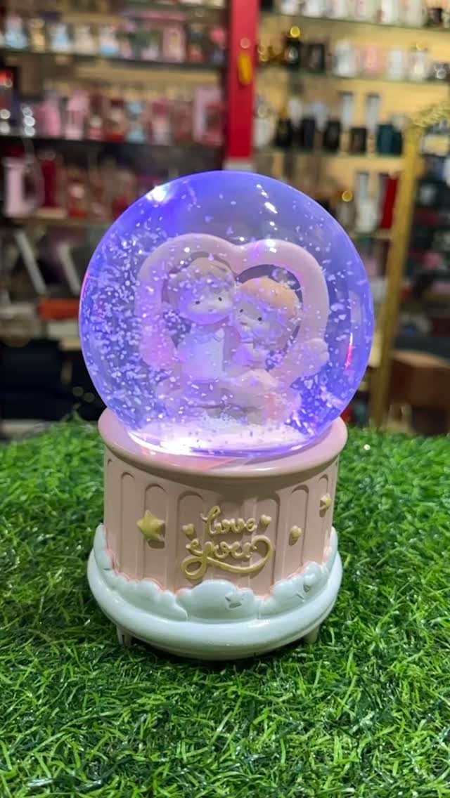 Glowing purple snow globe with a couple inside a heart on pink base.