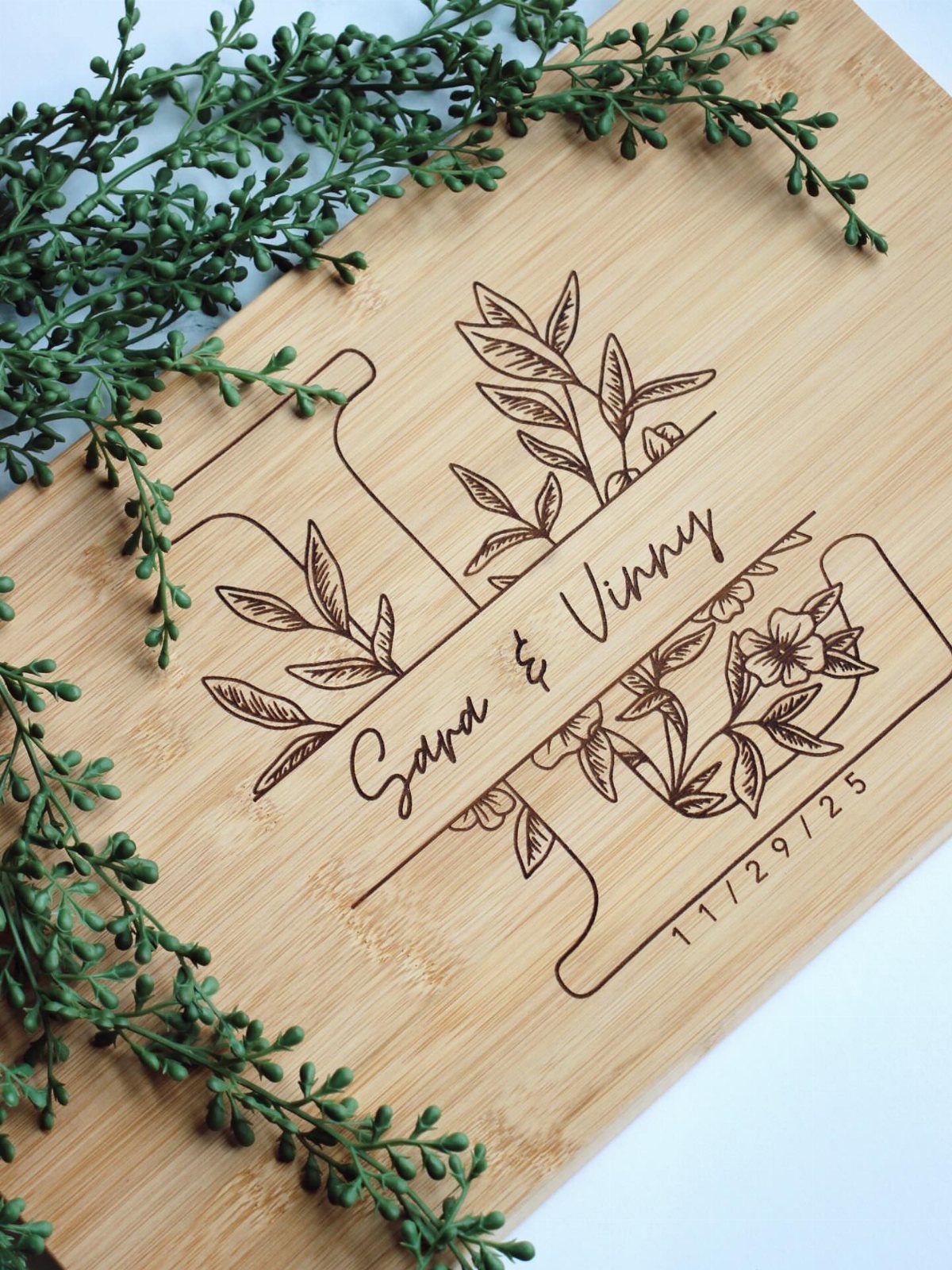 Engraved wooden cutting board with names Sara and Vinny and floral designs.