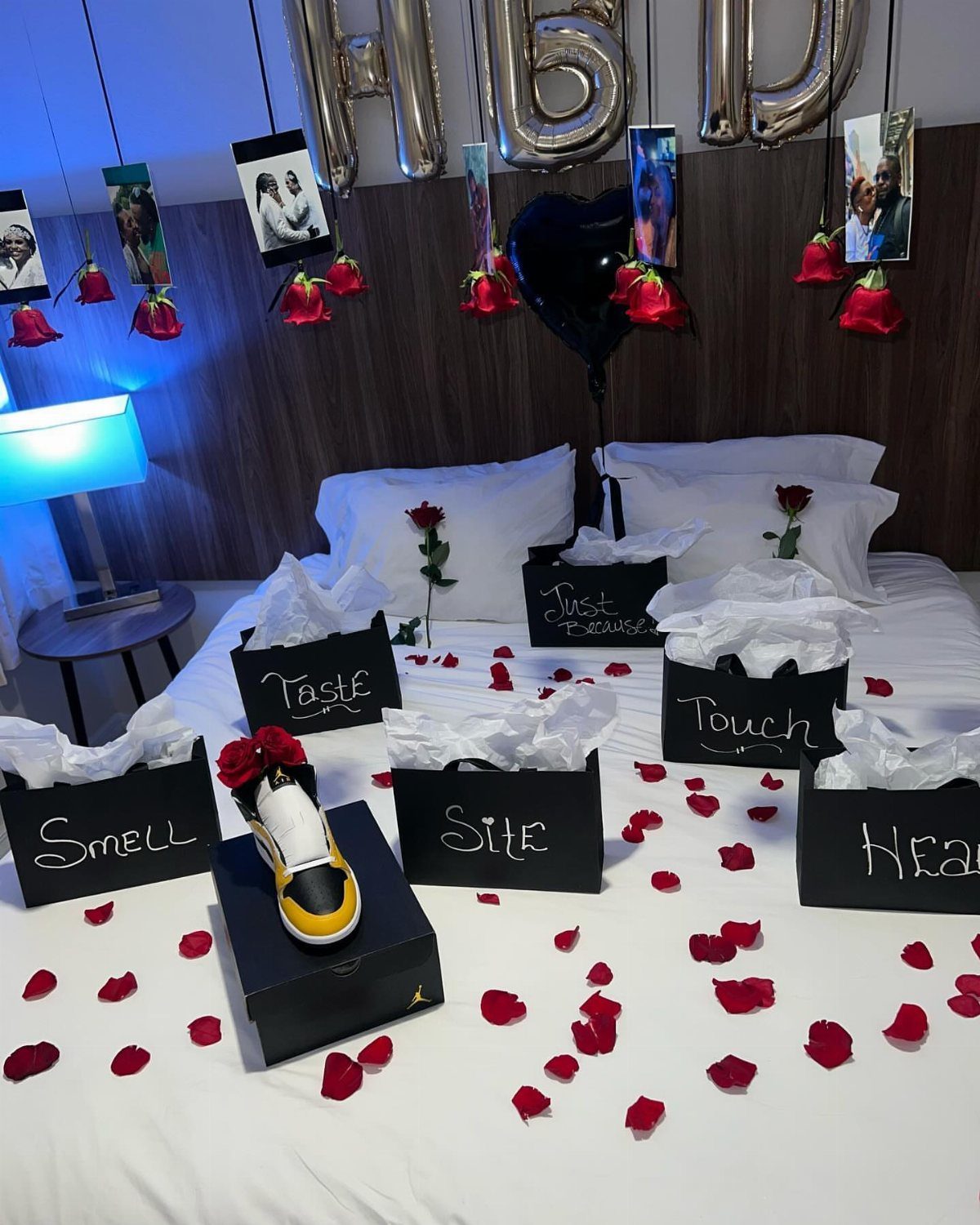 Bed decorated with rose petals, black gift boxes for five senses, and balloons.
