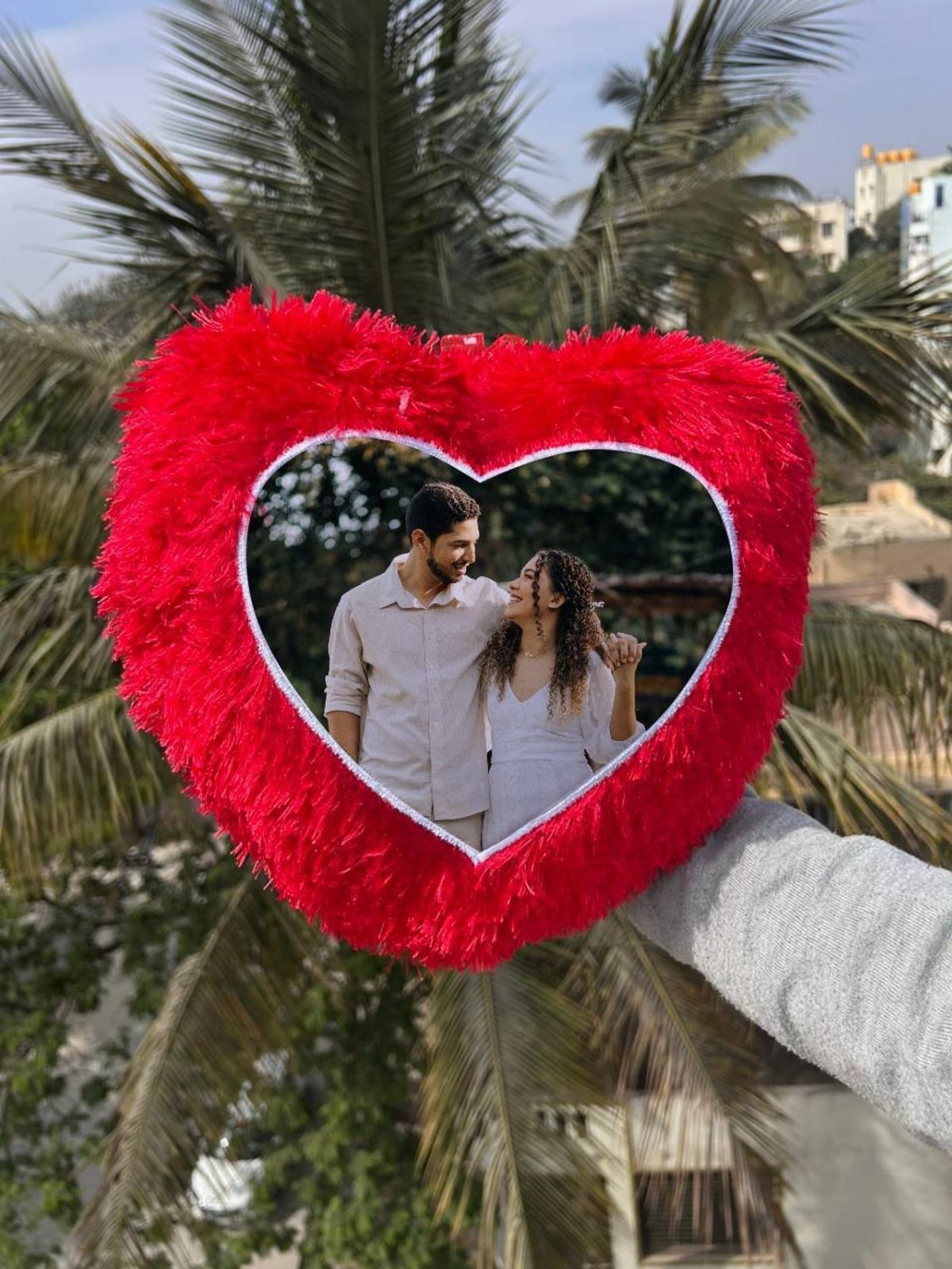 Red fluffy heart frame holding a photo of a couple against palm trees