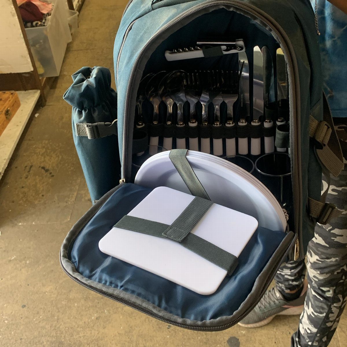Teal picnic backpack open to reveal plates, cutlery, and a small cutting board.