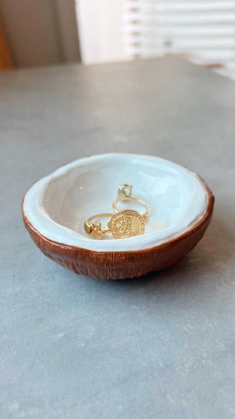 Small handmade clay bowl with white glaze and brown base holding gold rings.
