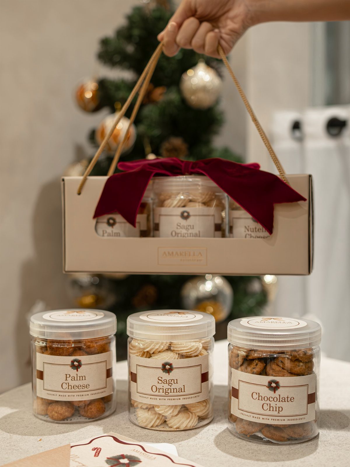 Three jars of assorted cookies in a gift carrier with a red bow.