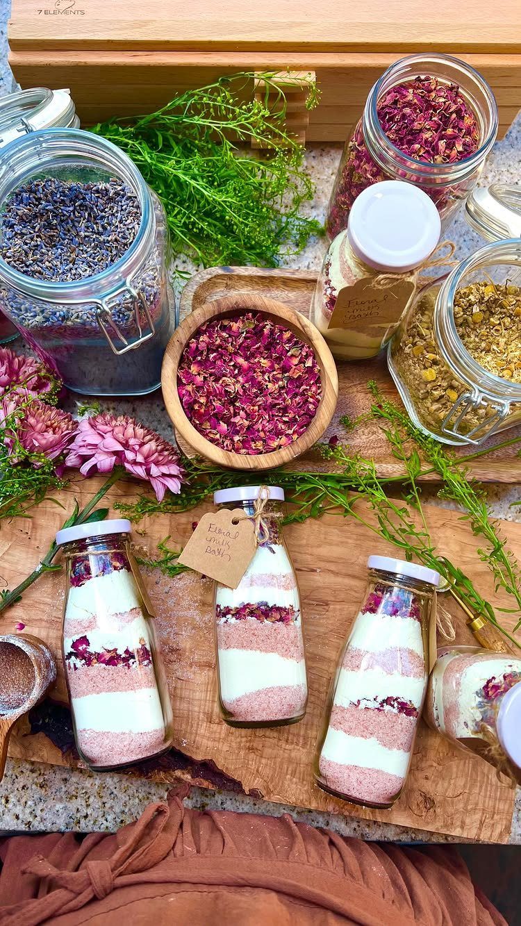 Layered pink and white bath salts in small glass bottles with dried petals.
