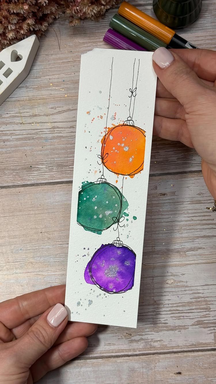 Handmade paper bookmark with colorful watercolor Christmas ornaments on a wooden background
