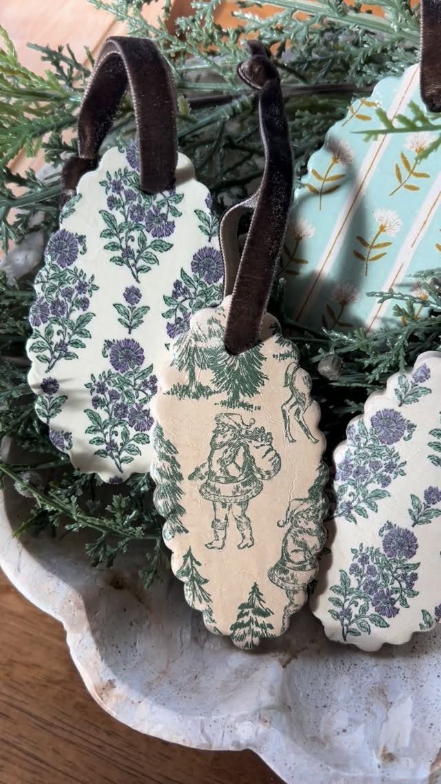 Vintage-style oval ornaments with velvet ribbons resting in a bowl of pine needles.