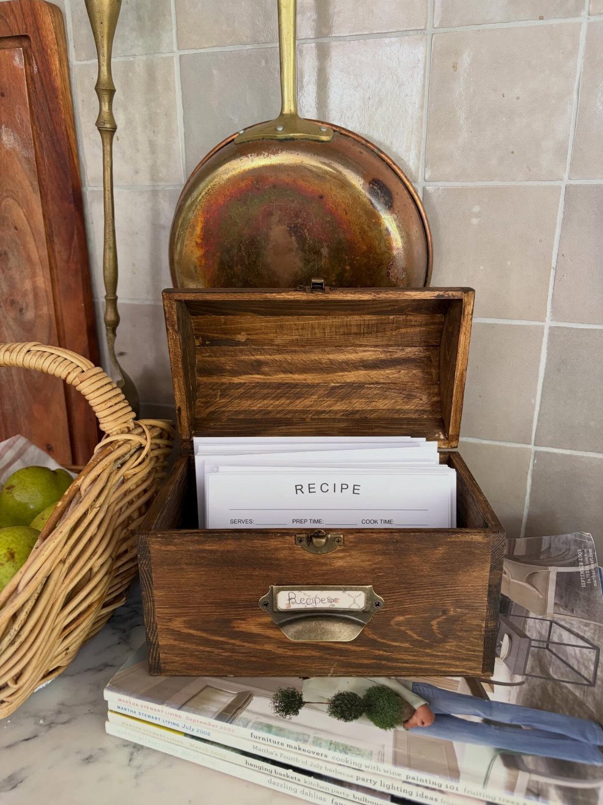 Wooden recipe box filled with white cards on a kitchen counter with copperware.
