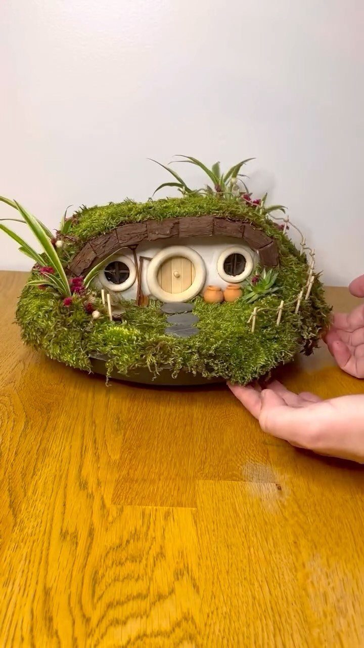 Handcrafted moss fairy house with a round door on a wooden table.