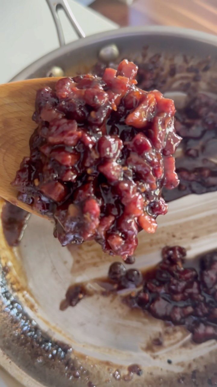 Wooden spoon holding a scoop of homemade dark red fruit jam from a pan
