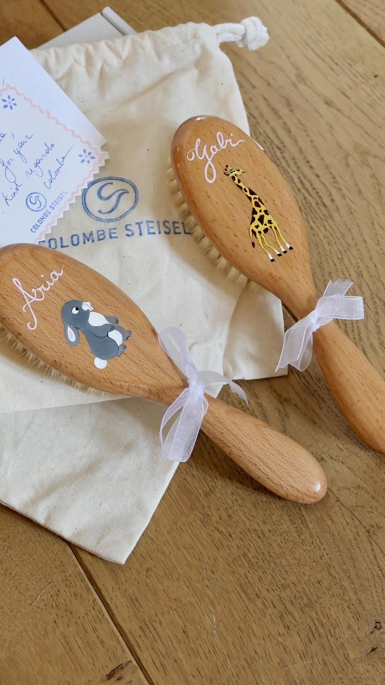 Two personalized wooden baby brushes with animal art resting on a canvas bag.