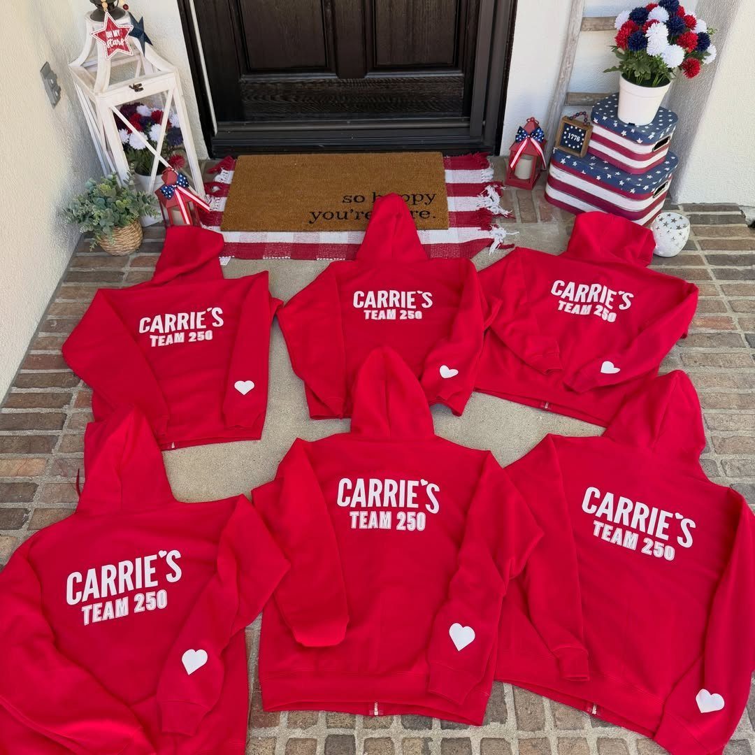 Six red hoodies with white team text laid out on a stone porch.