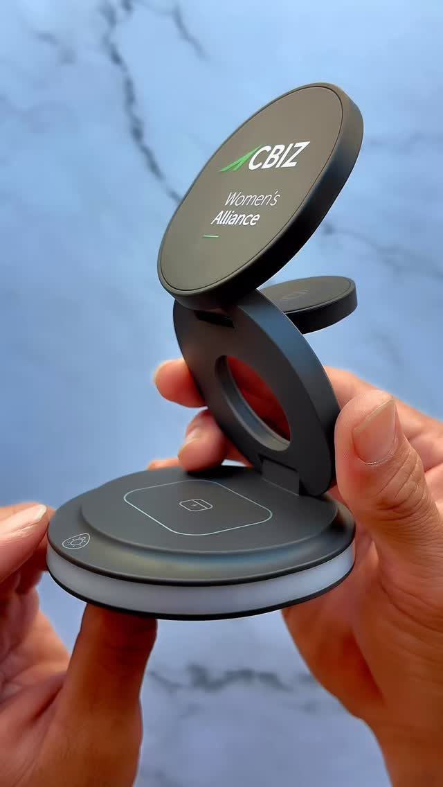 Black wireless charging station with CBIZ logo held by two hands over marble.