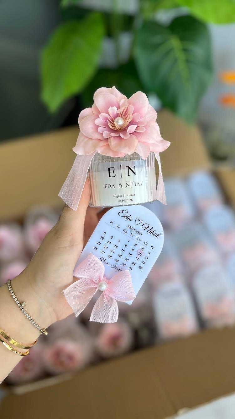 Small white candle jar with pink flower and calendar tag as party favors.
