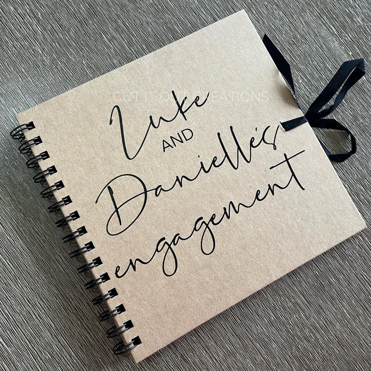 Spiral-bound kraft paper guest book for Luke and Danielle's engagement with black ribbon.