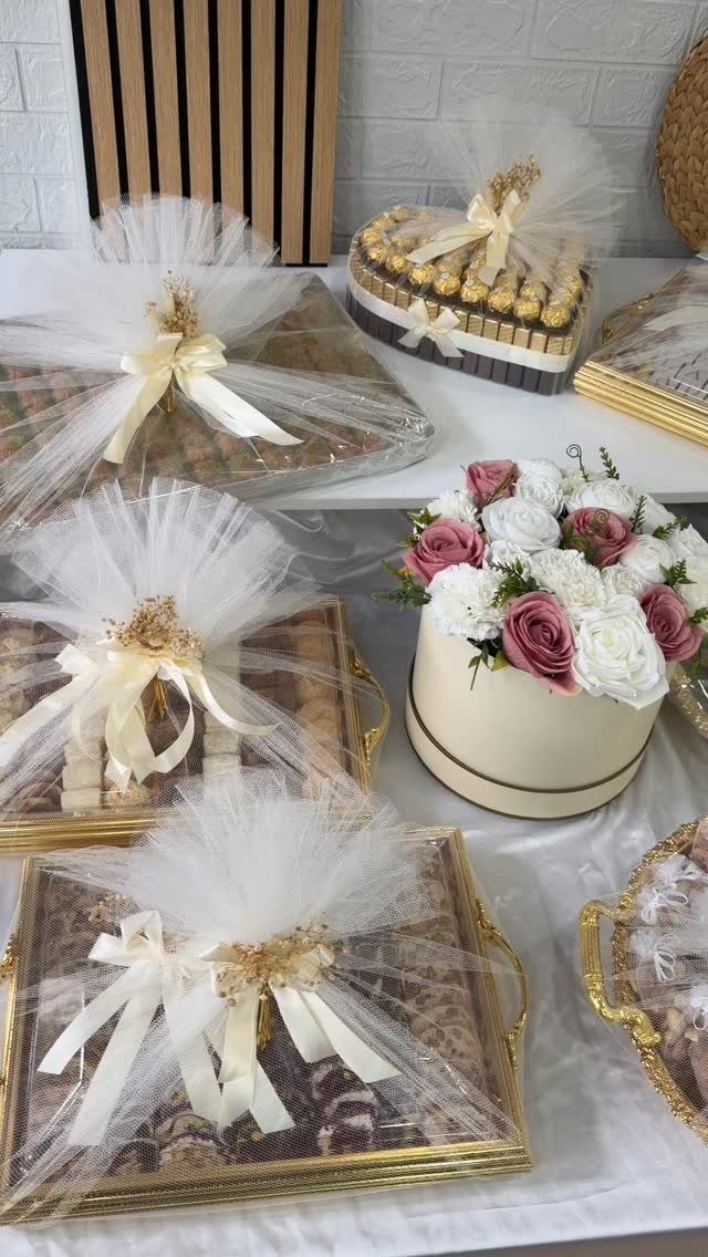 Gold-trimmed gift trays wrapped in tulle and a box of pink and white roses.