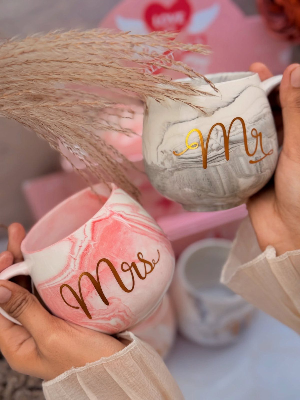 Two marble-patterned mugs with gold Mr. and Mrs. lettering held by hands.