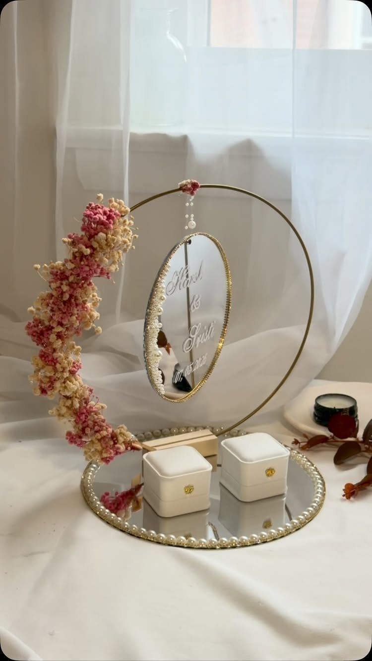 Gold circular ring holder with pink flowers, oval mirror, and two white boxes.