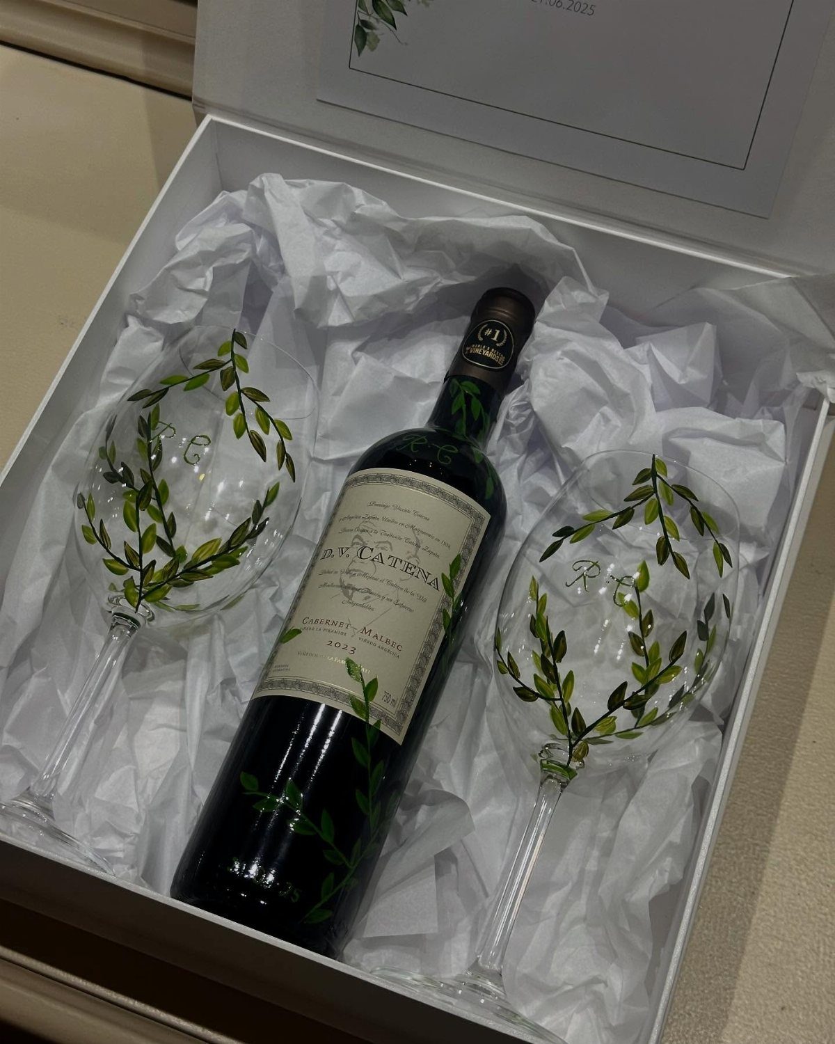 Bottle of red wine and two decorated glasses in a white gift box.