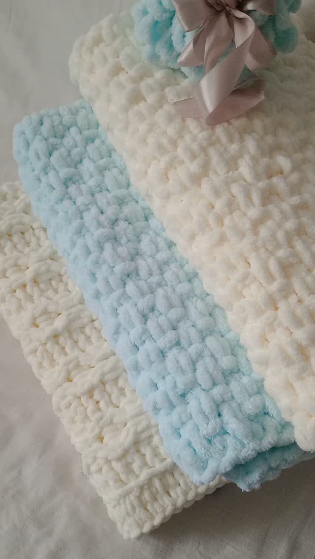 Folded white and light blue chunky knit blankets tied with a satin ribbon.