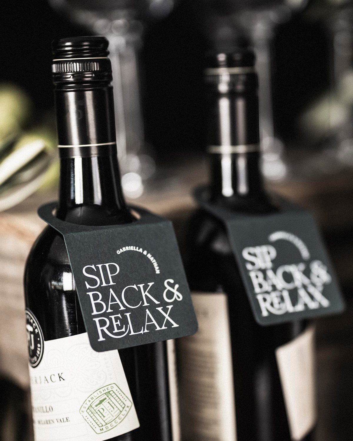 Two wine bottles with black gift tags reading Sip Back & Relax.