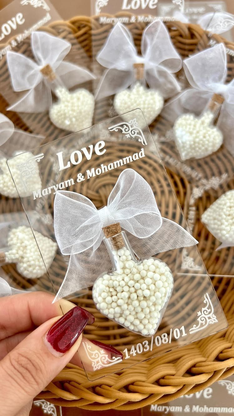 Heart-shaped pearl ornaments with white bows and personalized tags in a wicker basket.
