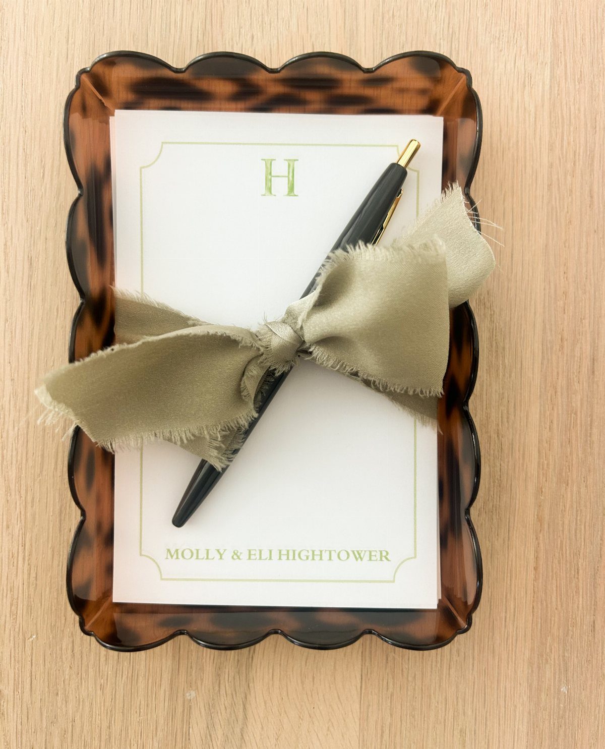 Personalized notepad and pen on a tortoiseshell tray with an olive green ribbon.