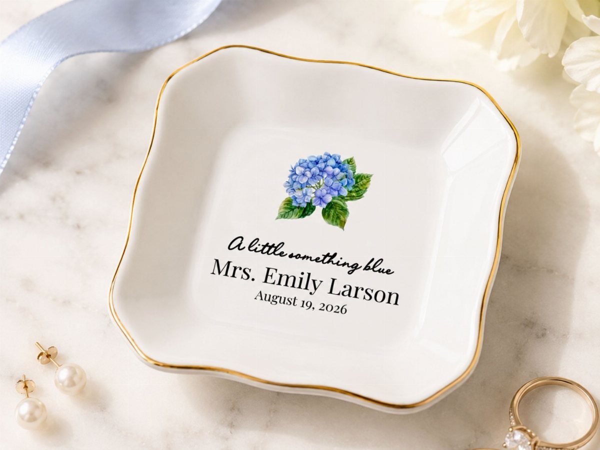 Personalized white ceramic ring dish with blue hydrangea and gold rim on marble.