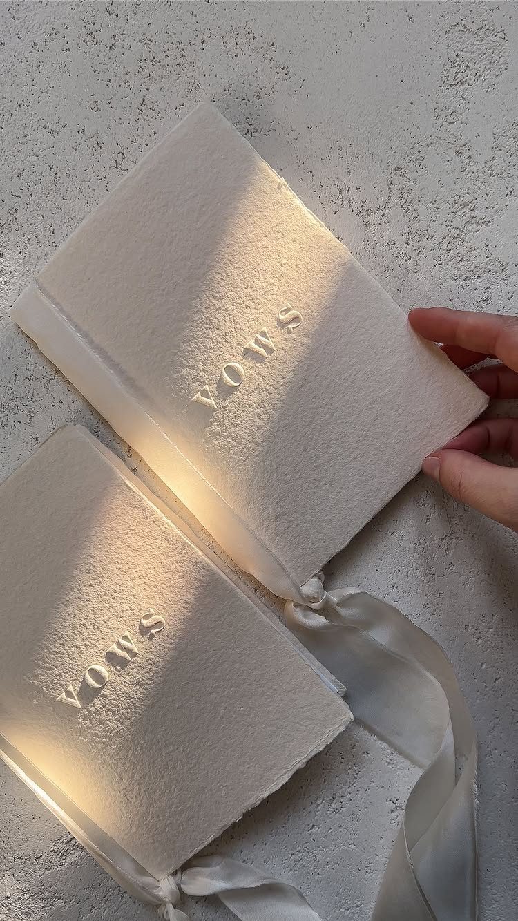 Two white textured vow books with embossed lettering and white satin ribbons.