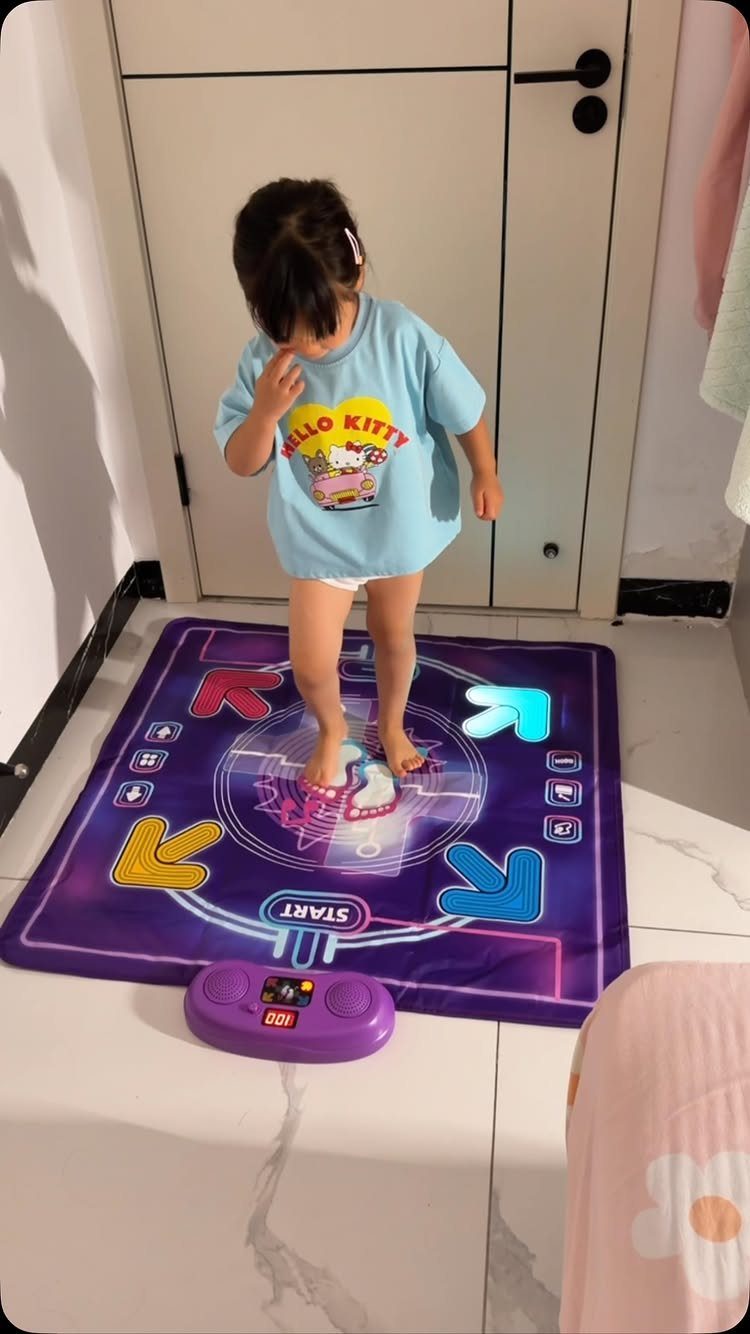 Young child standing on a purple electronic dance mat with colorful arrows indoors.