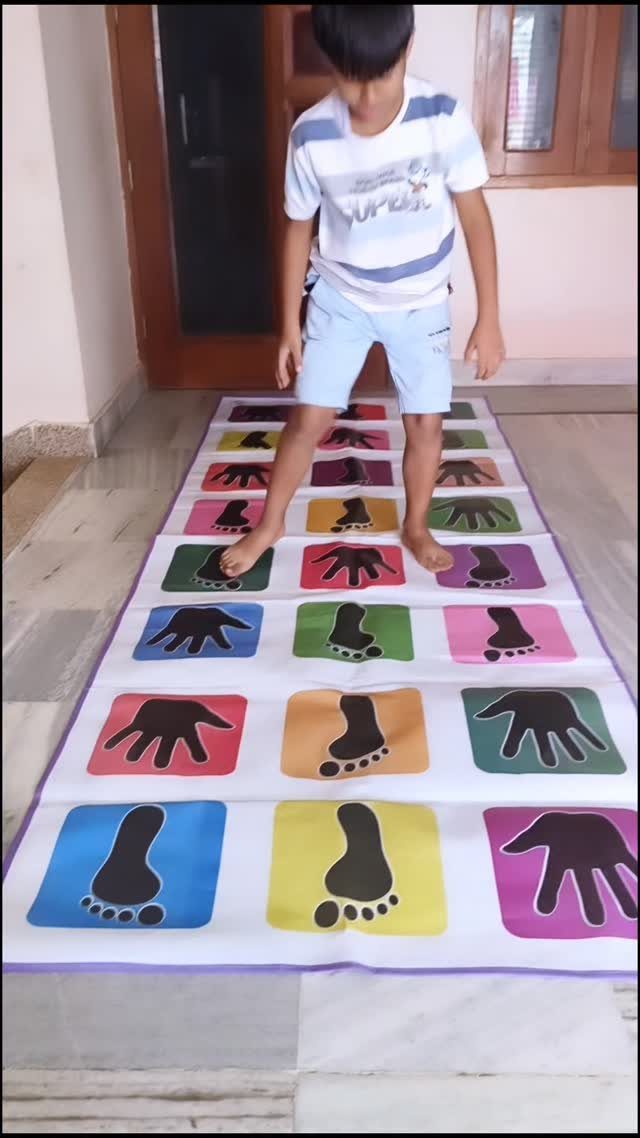 Boy standing on a colorful hand and foot print game mat indoors.