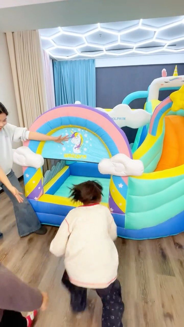 Colorful inflatable rainbow bounce house with a slide and children playing inside.