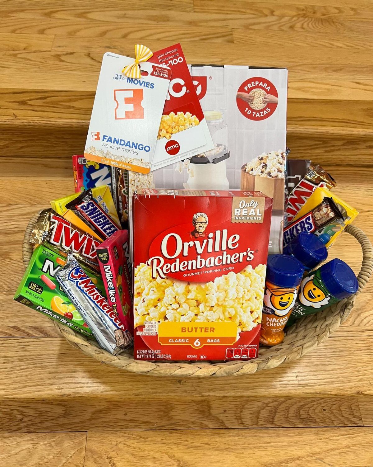Wicker gift basket filled with popcorn, assorted candies, and movie ticket vouchers.