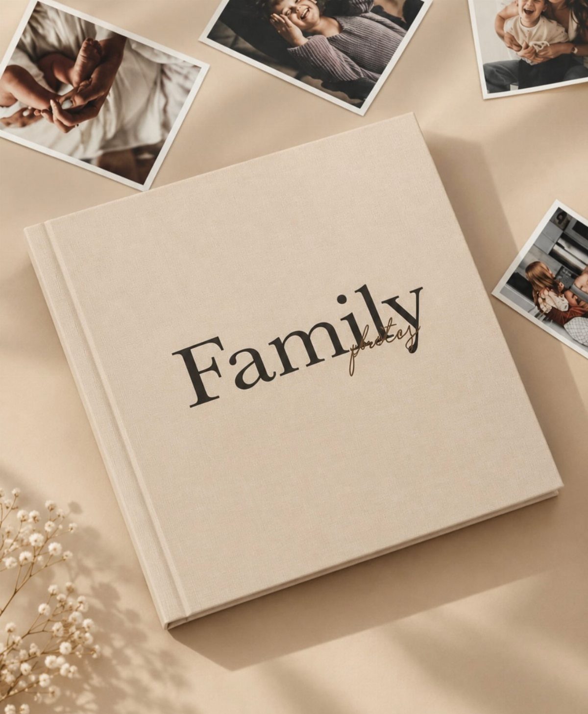 Beige family photo album surrounded by printed photographs and white baby's breath flowers.
