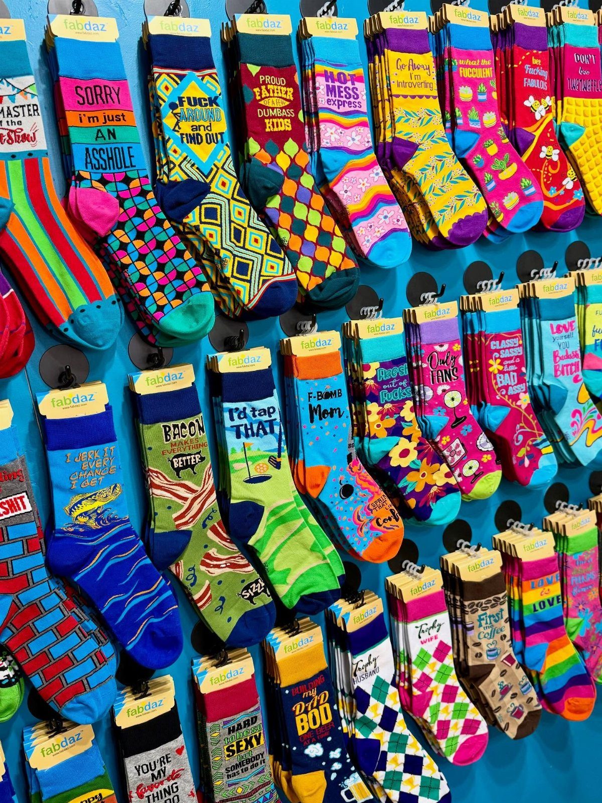 22 Gift Ideas for Brother, From Hoodies to Gadgets 7 Colorful patterned socks with funny text hanging on a bright blue display wall.