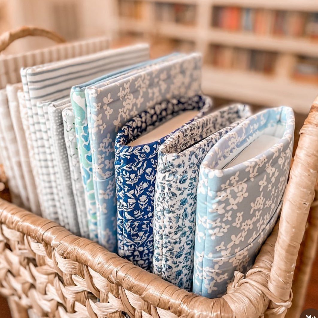Fabric book sleeves in blue and white patterns inside a woven wicker basket.