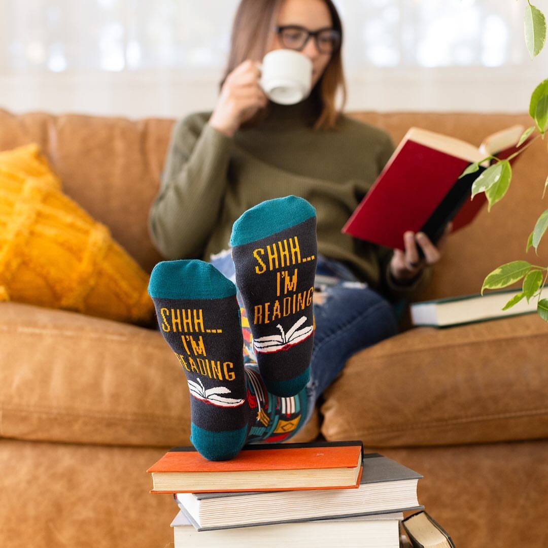 Blue socks with reading text resting on a stack of books on a sofa