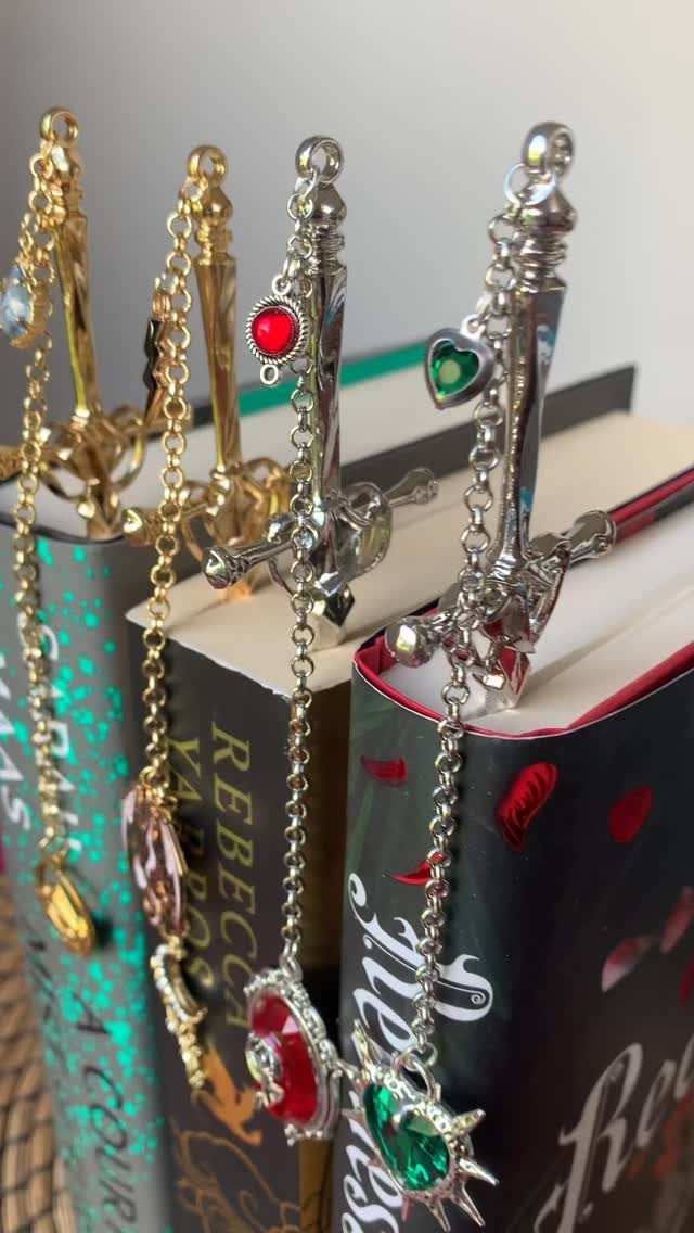 Sword-shaped metal bookmarks in gold and silver resting on hardcover books.