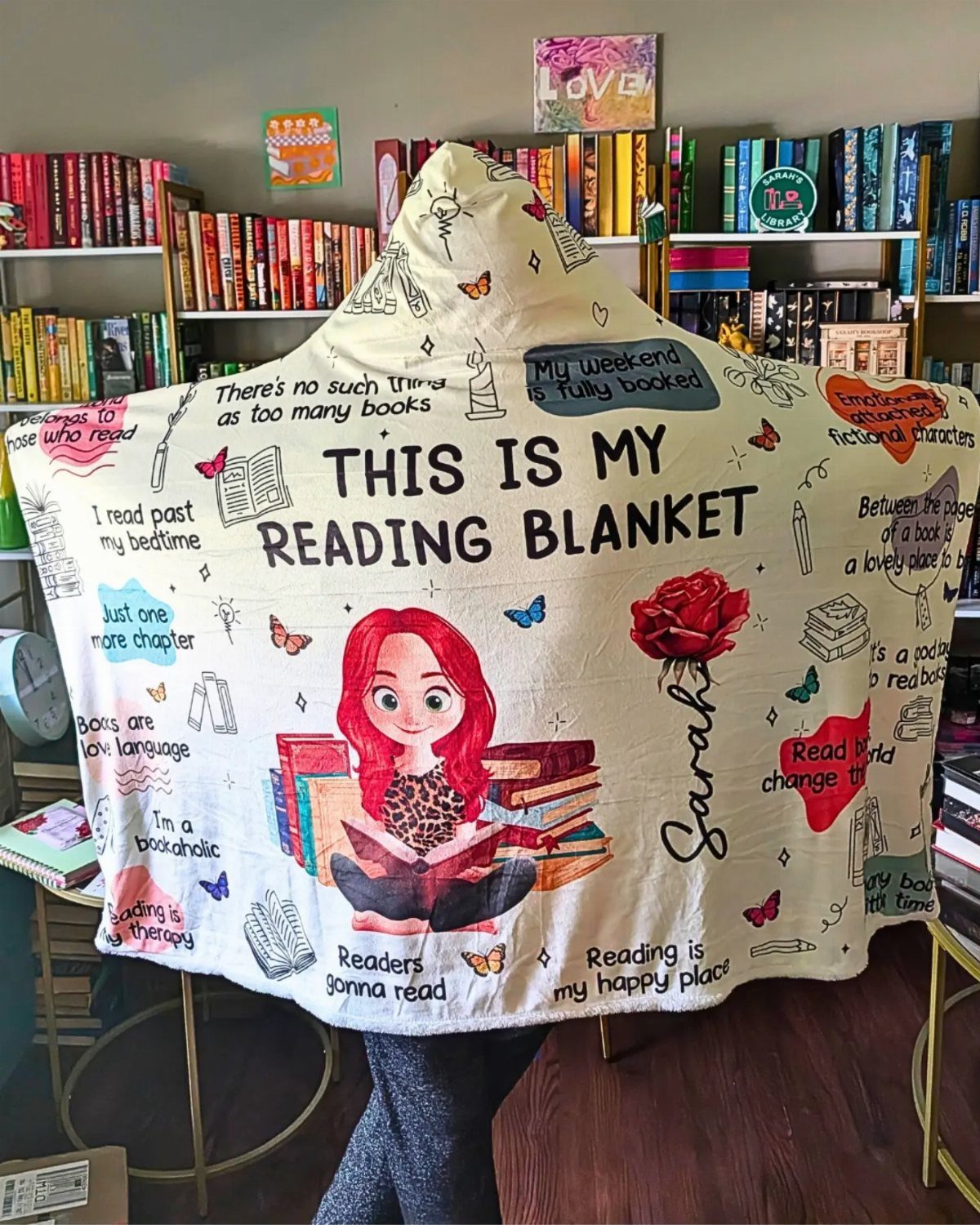 White hooded reading blanket with book-themed illustrations and quotes in a home library.